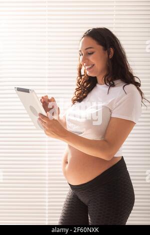 Bonne enceinte jeune belle femme parlant à son mari en utilisant la connexion vidéo et la tablette. Concept de communication et attitude positive pendant Banque D'Images