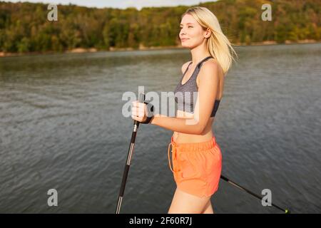 Femme sportive faisant marche nordique dans la nature au bord du lac pour la forme physique et l'endurance Banque D'Images