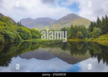 Paysage de montagne idyllique, verdoyant et verdoyant, reflet sur un Torren Lochan calme lors d'une journée d'été à Glencoe dans les Highlands écossais, en Écosse. Banque D'Images