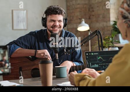 Jeune homme dans un casque assis avec de la guitare et donnant un entretien avec un dj radio en studio Banque D'Images