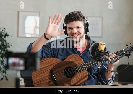 Portrait d'un homme adulte dans un casque souriant à l'appareil photo agitant ses mains et jouant de la guitare Banque D'Images