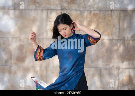 Jeune fille asiatique vietnamienne souriante dansant avec du bleu traditionnel robe avec des détails orange et jaune dans les rues de Madrid dans un et naturel Banque D'Images