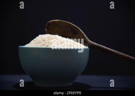 Poêle en porcelaine avec riz blanc cru et cuillère en bois sur fond noir. Riz blanc. Nourriture humaine. Céréales riches en amidon et source de nutriments. Culina Banque D'Images