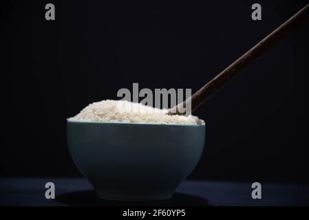 Poêle en porcelaine avec riz blanc cru et cuillère en bois sur fond noir. Riz blanc. Nourriture humaine. Céréales riches en amidon et source de nutriments. Culina Banque D'Images