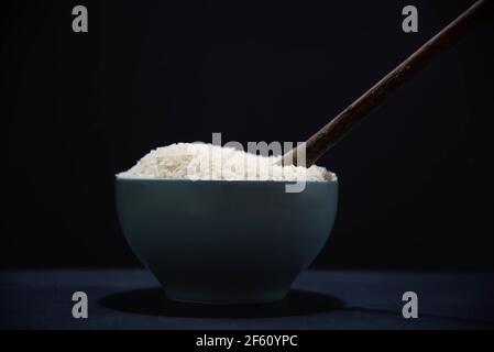 Poêle en porcelaine avec riz blanc cru et cuillère en bois sur fond noir. Riz blanc. Nourriture humaine. Céréales riches en amidon et source de nutriments. Culina Banque D'Images