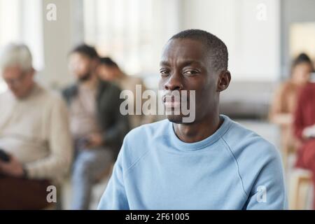 Portrait d'un homme afro-américain sérieux regardant la caméra tout en étant assis dans le public avec divers groupes de personnes en arrière-plan, espace de copie Banque D'Images