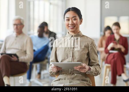 Portrait d'une femme d'affaires asiatique réussie souriant à l'appareil photo tout en posant au bureau avec des gens en arrière-plan, espace de copie Banque D'Images