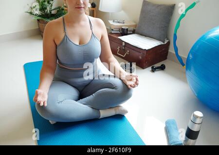 S'adapte jeune femme de taille plus méditant dans la position de lotus sur tapis de yoga à la maison Banque D'Images