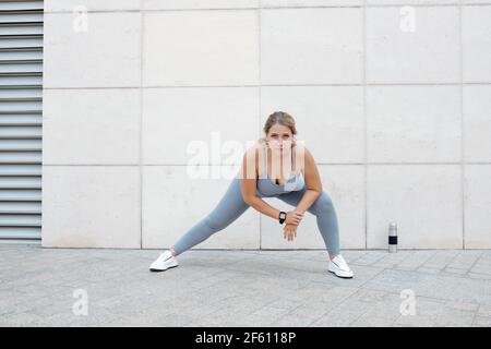 Jeune femme fatiguée, malheureuse et de taille plus, qui fait des fentes latérales et se penche vers l'avant pour ouvrir les hanches serrées et l'aine, tout en renforçant la cuisse intérieure et les fessiers Banque D'Images