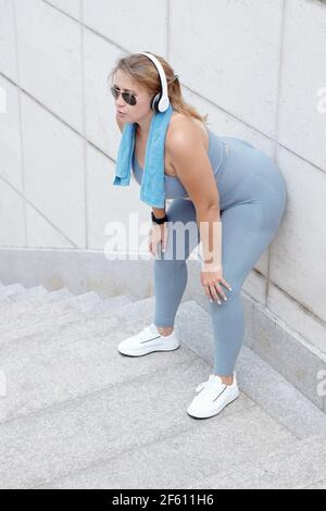 Taille plus fatiguée jeune femme penchée sur le mur de repos après avoir fait du jogging à l'extérieur le matin Banque D'Images