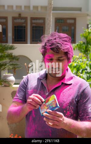 Jeune indien couvert de poudre colorée ouvrant un paquet de couleurs bio à base de plantes pendant le festival hindou de couleur holi Banque D'Images