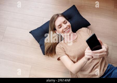 Jeune femme joyeuse se reposant sur le sol et filant ami ou petit ami, vue d'en haut Banque D'Images