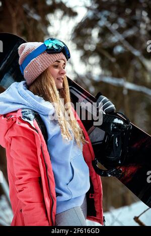 Femme snowboarder en costume brillant dans des lunettes de sport tient un snowboard. Sports extrêmes. Loisirs Banque D'Images