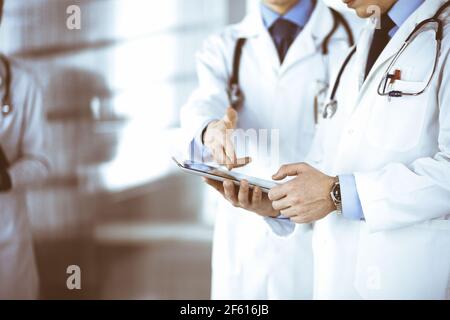 Un groupe de médecins inconnus utilise une tablette pour vérifier certains dossiers médicaux, tout en se tenant dans un bureau d'hôpital. Médecins prêts à Banque D'Images