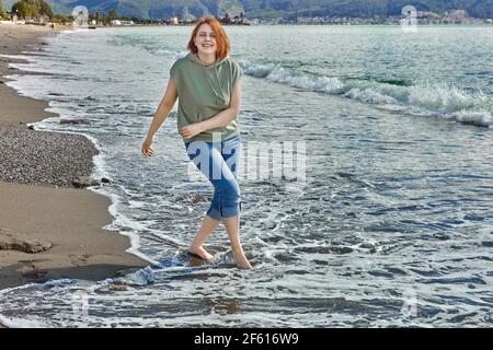 Une jeune femme sur la plage de la station turque de Fethiye au printemps mois de mars marche pieds nus le long de la ligne de surf. Banque D'Images