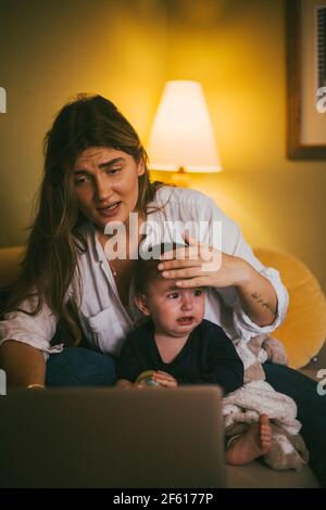 Mère avec bébé fille prenant des conseils par appel vidéo sur pc portable à la maison Banque D'Images