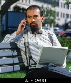 WASHINGTON, DC, Etats-Unis - l'homme parle du téléphone mobiloe relié à l'ordinateur Compaq à l'aide d'un modem sans fil, sur banc de parc. Banque D'Images