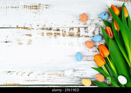 Les Pâques multicolores ont peint des œufs mouillés dans un panier sur une table en bois blanc avec des tulipes. Composition traditionnelle du printemps éléments de Pâques fleurs et oeufs pour le printemps. Décoration de printemps concept Banque D'Images