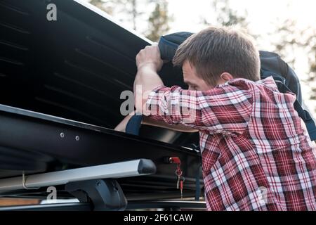 L'homme met des choses dans le porte-bagages de toit d'une voiture ou dans une caisse, lors d'une soirée d'été. Voyage en famille. Banque D'Images