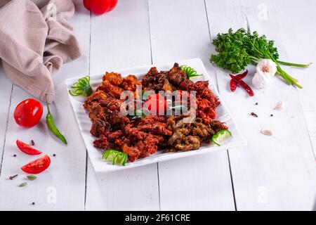 Pakoda de poulet ou pakora, trois saveurs différentes de pakora disposées dans une assiette carrée blanche et garnie de tomates et de concombres placé sur blanc te Banque D'Images