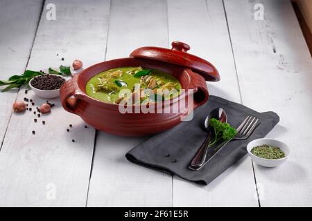 Curry de poulet vert avec ingrédients crus qui est disposé dans un matériel de terre avec fond blanc. Banque D'Images