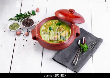 Curry de poulet vert avec ingrédients crus qui est disposé dans un matériel de terre avec fond blanc. Banque D'Images