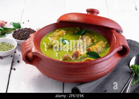 Curry de poulet vert avec ingrédients crus qui est disposé dans un matériel de terre avec fond blanc. Banque D'Images
