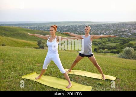 Couple d'âge moyen faisant cinq étoiles pointues asana tout en pratiquant yoga ensemble sur une colline herbeuse Banque D'Images