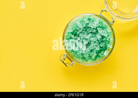 Sel de bain aromatique vert dans un pot en verre sur fond jaune. Spa, concept de soins de la peau. Vue de dessus, espace de copie. Mise au point sélective Banque D'Images