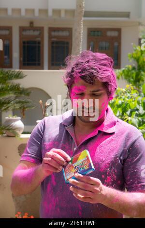 Jeune indien couvert de poudre colorée ouvrant un paquet de couleurs bio à base de plantes pendant le festival hindou de couleur holi Banque D'Images