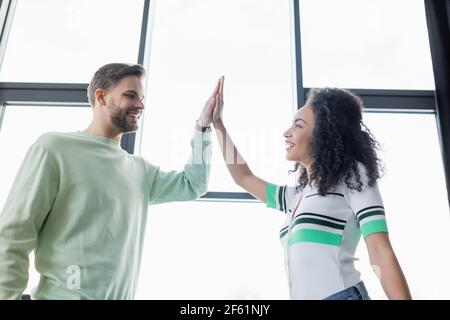 vue en contre-plongée des jeunes collègues d'affaires interraciaux qui ont réussi à donner cinq hauts au bureau Banque D'Images