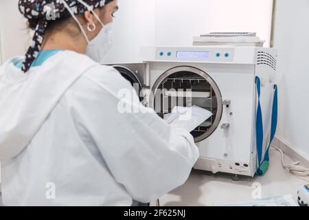 L'assistant du dentiste insère l'instrument dentaire emballé dans l'autoclave pour le stériliser. Équipements dentaires modernes. Banque D'Images