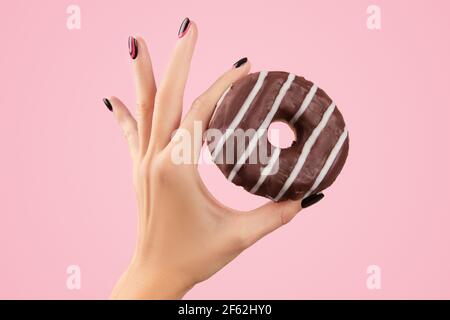 Main des femmes tenant le donut coloré sur fond rose Banque D'Images