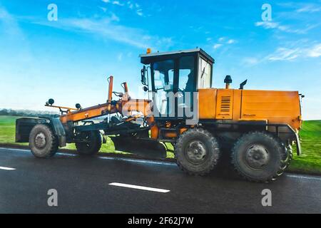 Le racleur de la route roule sur un asphalte contre la prairie verte et le ciel bleu. Transport industriel, voiture. Banque D'Images