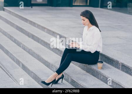 Photo de la taille du corps pleine longueur de la femme d'affaires faisant le projet sur ordinateur portable freelance assis dans le port formel stilettos boire du café Banque D'Images