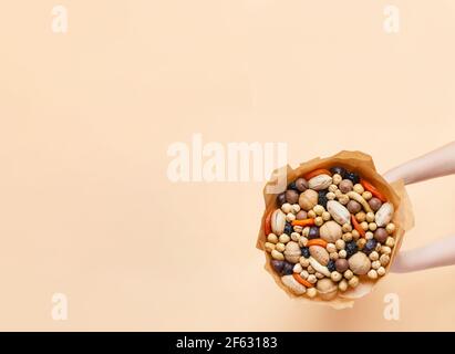 Les mains tiennent un bouquet de noix, de fruits secs : pruneaux, prunes, abricots sur fond beige Banque D'Images
