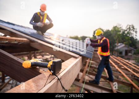 Mise au point sélective Outils de couverture, travailleur de toiture utilisant une perceuse électrique installer sur la nouvelle tôle de toit au chantier de construction. Banque D'Images