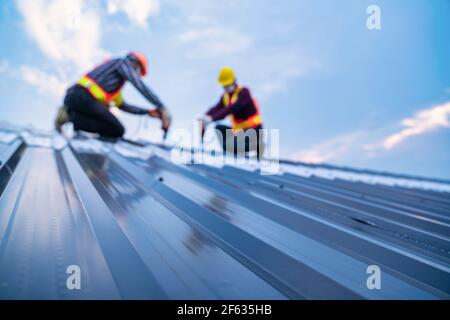 Toit sélectif de mise au point, vêtements de sécurité pour les ouvriers de construction à l'aide d'outils de forage électrique installer sur la nouvelle tôle de toit, concept de construction de toit. Banque D'Images