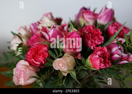 bouquets de roses, clous de girofle et tulipes dans un vase sur une table avec fond blanc et gris - gros plan Banque D'Images