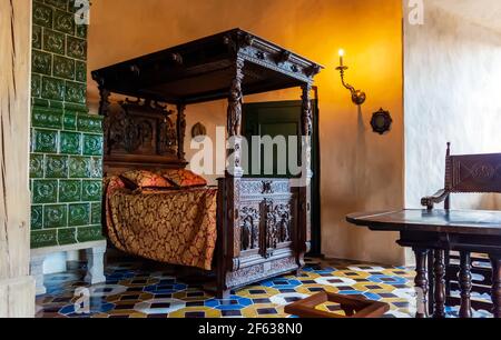 Intérieur du château de Bauska - Chambre duchesse avec carreaux de couleur sur le sol, lit d'essai sculpté et luxueux four Banque D'Images