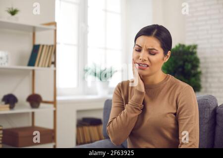 Jeune femme souffrant de maux de dents graves ou de sensibilité des dents au toucher sa joue Banque D'Images