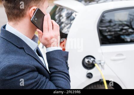 Homme chargé une voiture électrique et parlant sur le smartphone. Concept de voiture ECO EV Banque D'Images