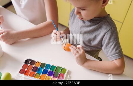 Deux enfants adolescents peignent des œufs de Pâques avec des couleurs pour préparer les vacances. Vue de dessus en gros plan Banque D'Images