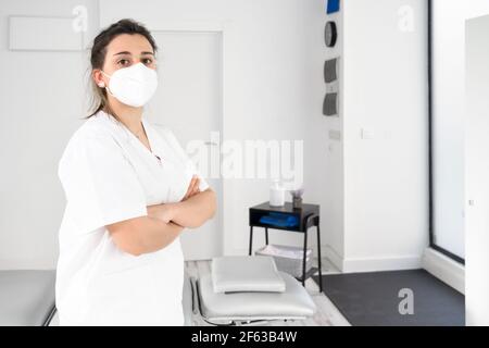 Physiothérapeute femme confiante posant dans une clinique moderne portant un masque facial protecteur pendant une pandémie de coronavirus. Photo de haute qualité Banque D'Images