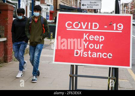 Londres, Royaume-Uni. 29 mars 2021. Les hommes marchent après un panneau indiquant 'COVID-19, gardez votre distance' à Londres. Credit: Dinendra Haria/SOPA Images/ZUMA Wire/Alay Live News Banque D'Images