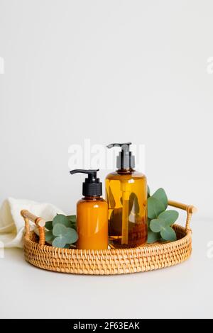Plateau en rotin avec bouteilles de shampooing ou gel douche en verre ambré, branches d'eucalyptus, serviette. SPA de cosmétiques biologiques naturels sur la table de bain Banque D'Images