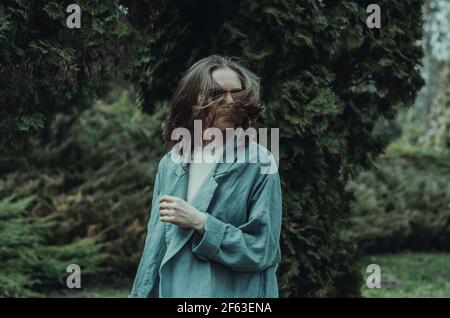 Femme tendance portant un gilet aqua et des lunettes de soleil se jetant les cheveux côte à côte, sur fond vert extérieur. Concept : mode durable et intemporel Banque D'Images