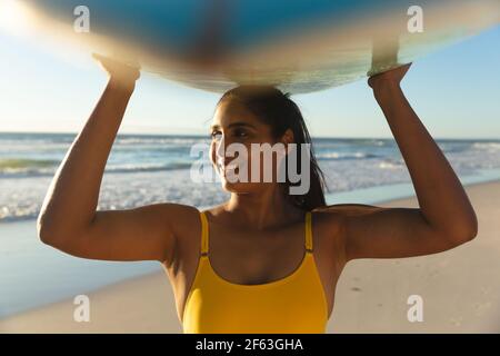 Bonne femme de course mixte sur la plage portant la planche de surf tête Banque D'Images