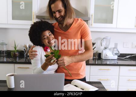 Joyeux couple divers assis dans la cuisine un homme lui donnant fleurs Banque D'Images