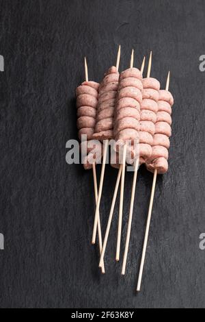 Saucisse spirale crue sur bâton de bois sur fond de pierre noire Banque D'Images